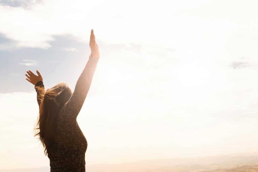 Person raising arms toward sunlight symbolizing hope, acceptance, and mindfulness in therapy