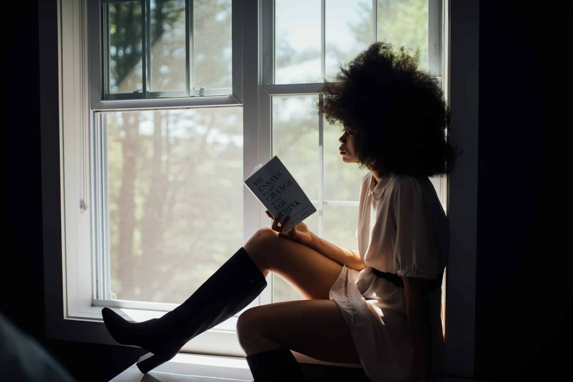 African American woman reading a book with sunlight obscuring her face, a quiet moment of focus and warmth