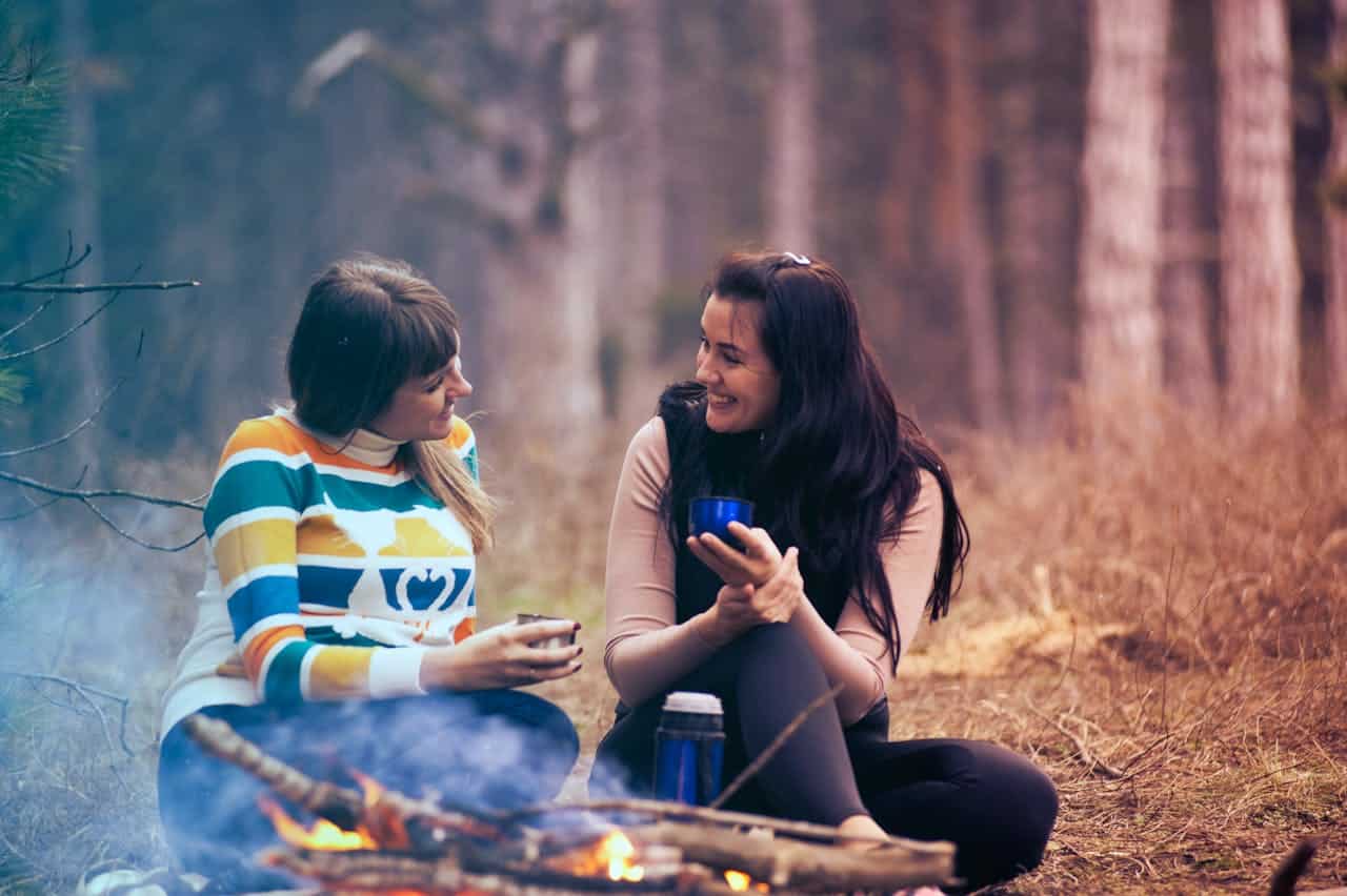 Two women talking warmly by a campfire, representing connection and interpersonal effectiveness in DBT therapy