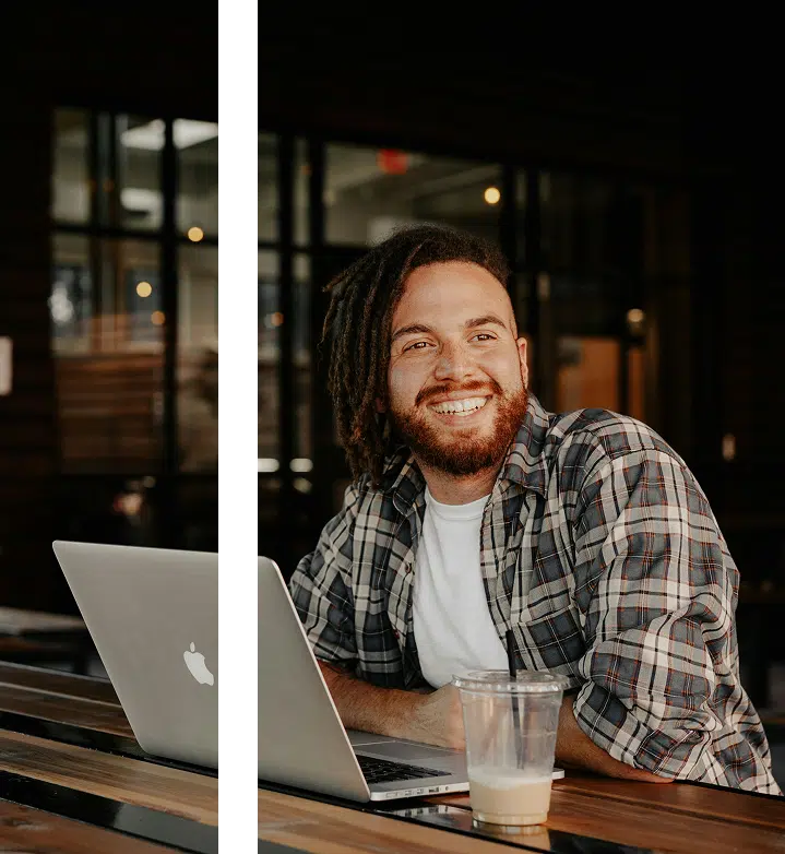 Man sitting in a café with coffee beside him and laptop open, smiling softly in a calm, everyday setting