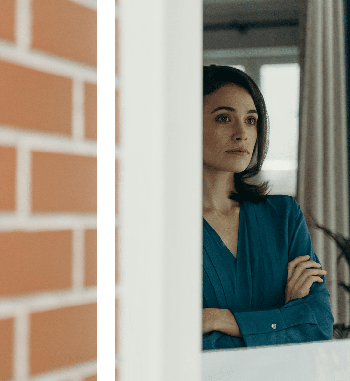 Woman in professional attire gazing out a window, reflective moment suggesting emotional processing and perspective