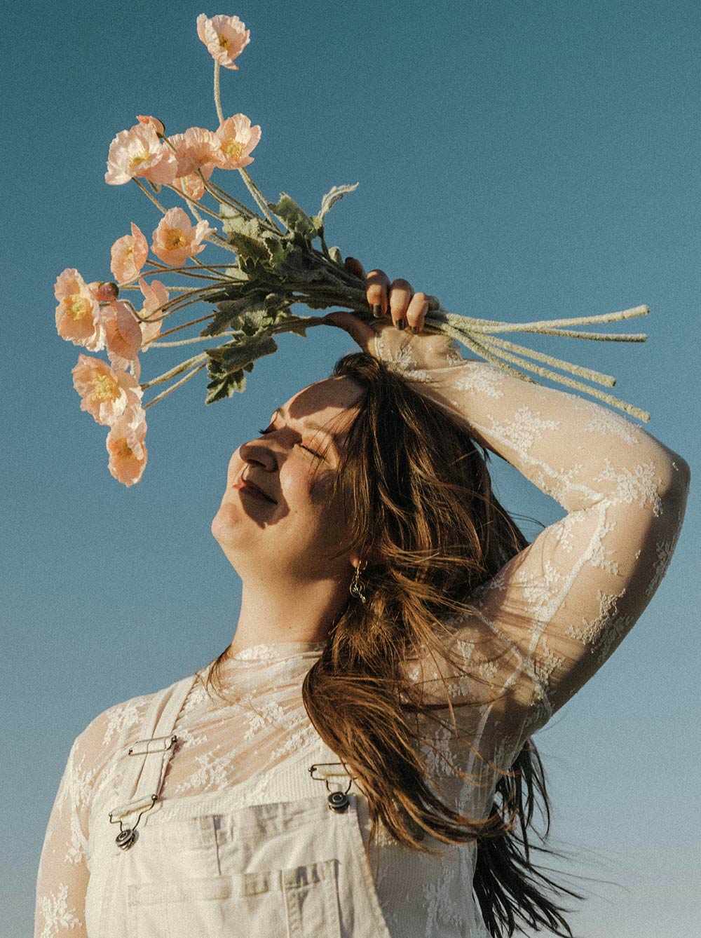 Woman holding flowers with eyes closed, facing sunlight, peaceful expression conveying gratitude and emotional openness