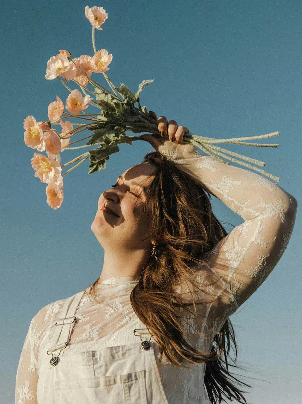 Woman holding flowers with eyes closed, facing sunlight, peaceful expression conveying gratitude and emotional openness