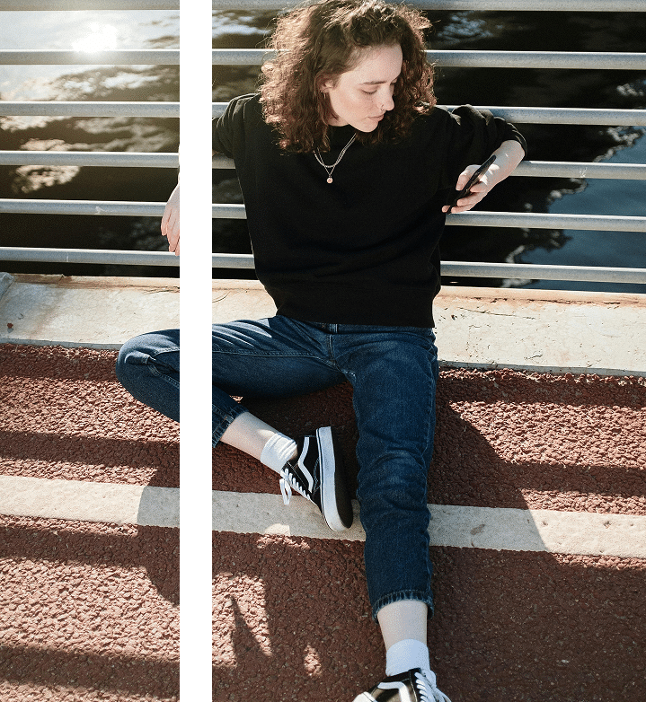 Woman seated near a fence looking at her phone, a casual moment reflecting everyday pause and awareness