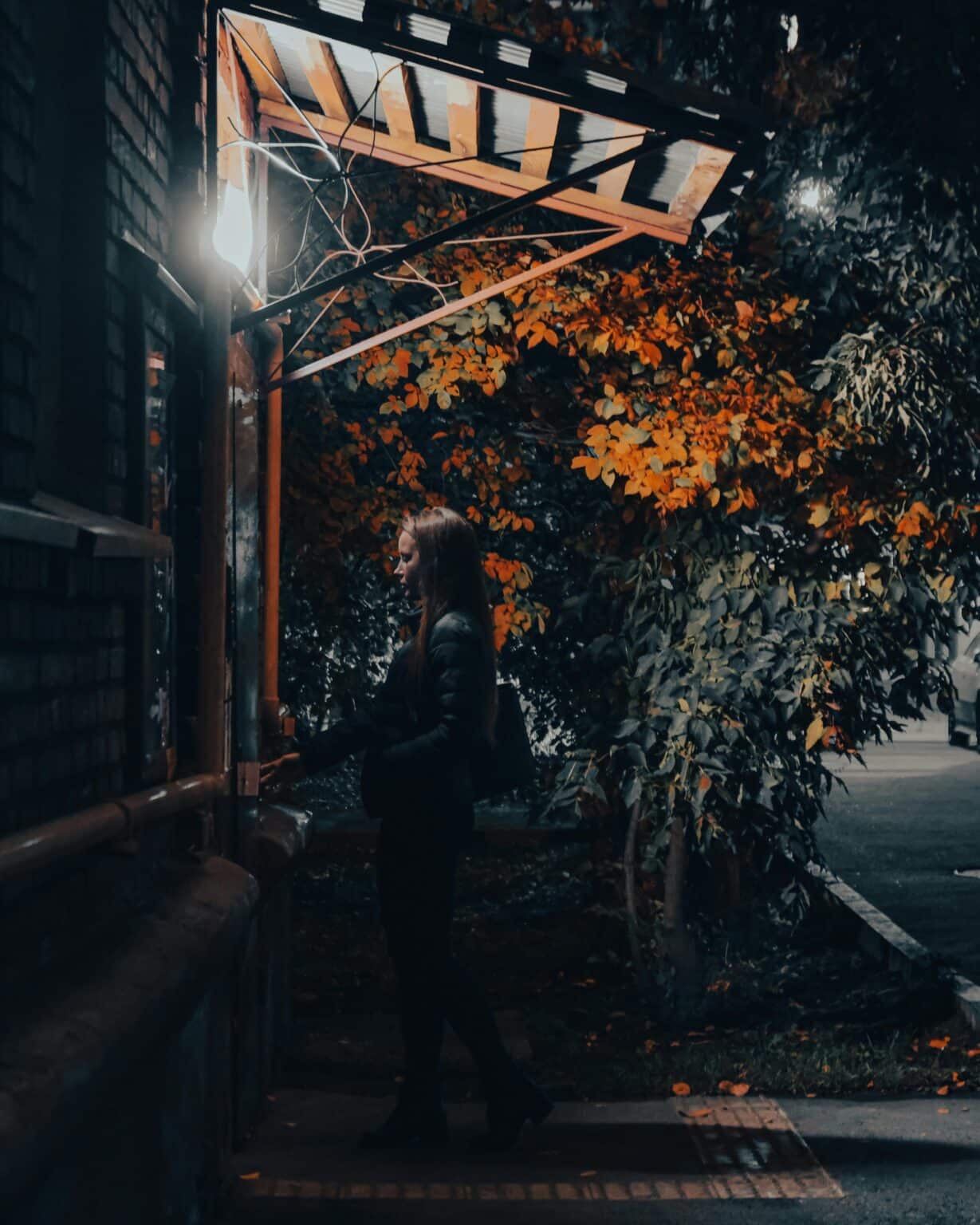 Woman walking alone on a dim street with orange leaves around her, quiet atmosphere suggesting introspection and transition