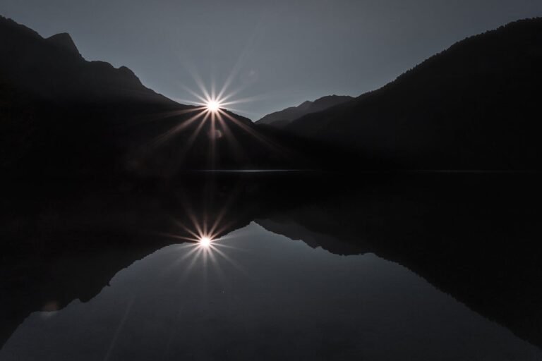 Sunrise between dark mountains reflected on calm water, symbolizing reflection and hope in depression therapy.