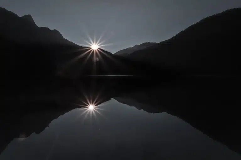 Sunrise between dark mountains reflected on calm water, symbolizing reflection and hope in depression therapy.