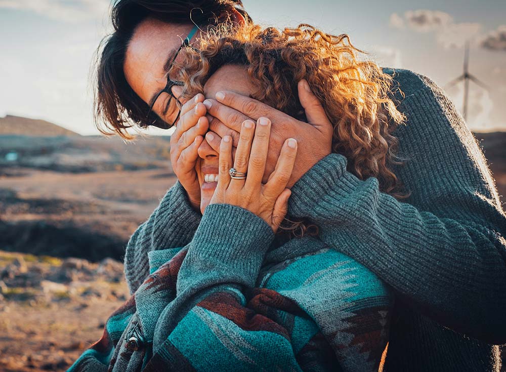 An Asian man playfully covering a woman’s eyes as she smiles