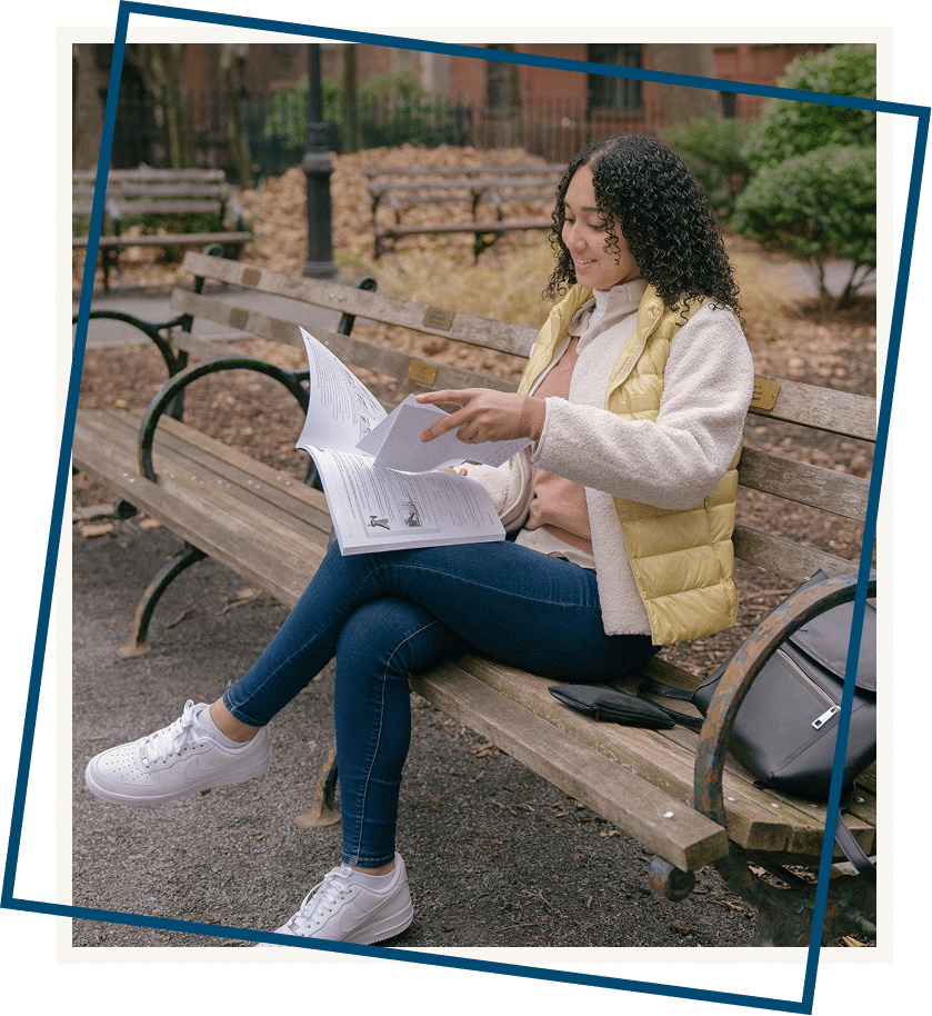 A girl sitting on a bench in a park reading a book