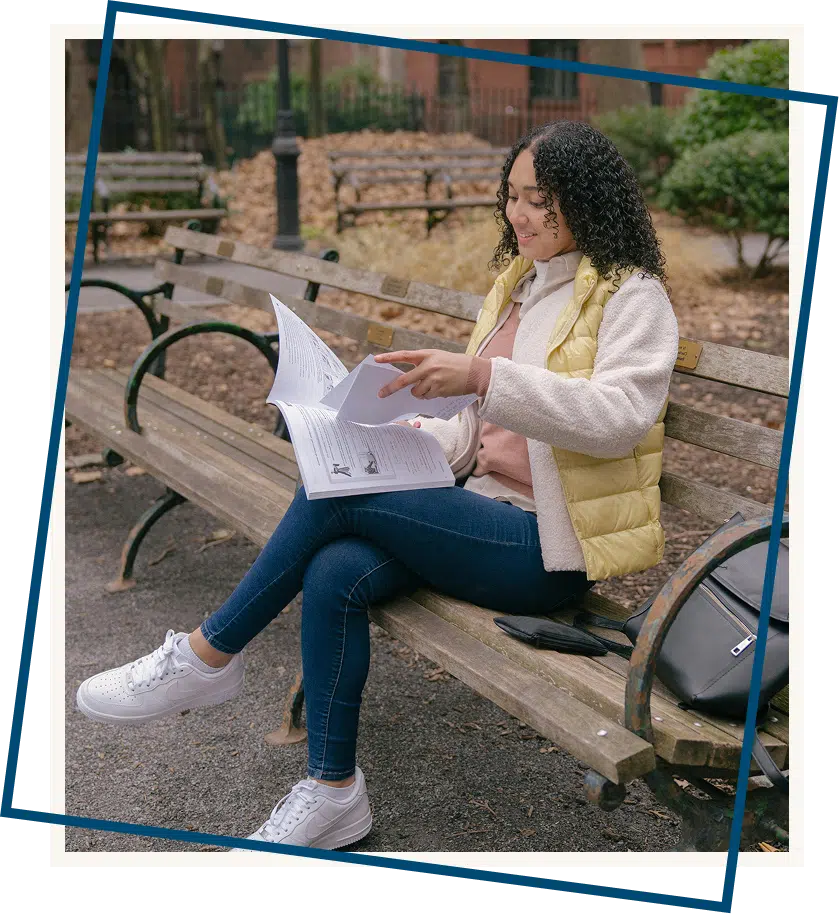 A girl sitting on a bench in a park reading a book