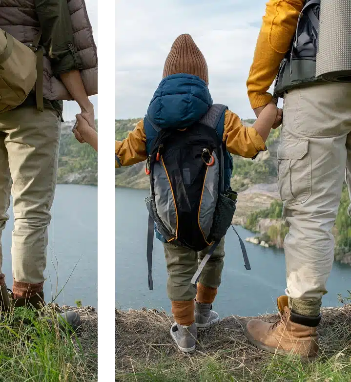  Family hiking with backpacks, holding hands beside a peaceful mountain lake, and a wide open sky together on a nature trip today