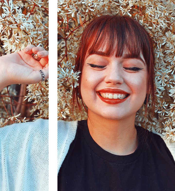 A girl smiling with her eyes closed, surrounded by white flowers in the background.