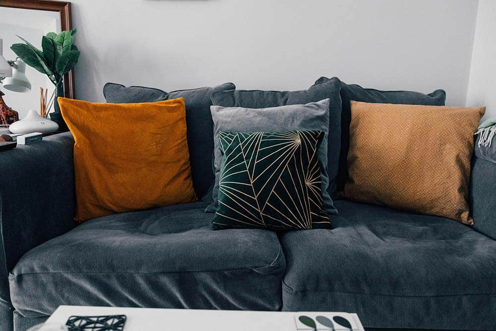 A dark grey sofa is decorated with four throw pillows in various colors and patterns