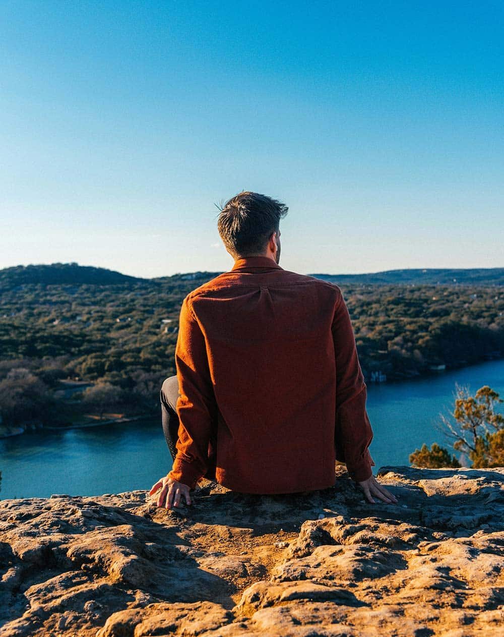  A man sitting at the edge of a mountain overlooking a river symbolizes reflection, clarity, and perspective.