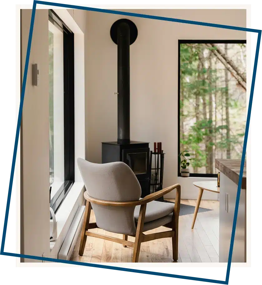 A cozy chair by a fireplace with large windows overlooking a peaceful natural view