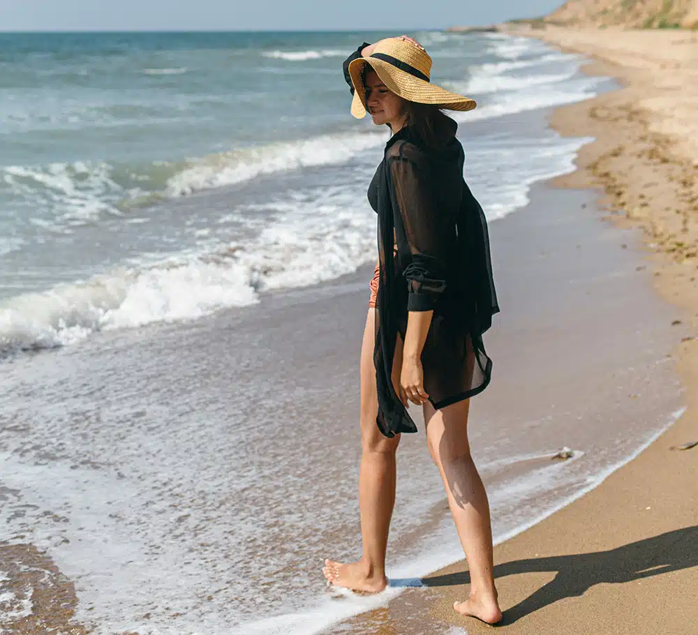 A woman wearing a beach hat is walking into the ocean, symbolizing release, renewal, and emotional freedom.