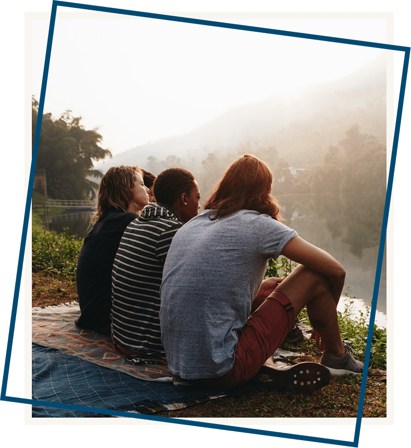 People sitting together on a rug by a peaceful lake, reflecting and connecting in a calm outdoor setting