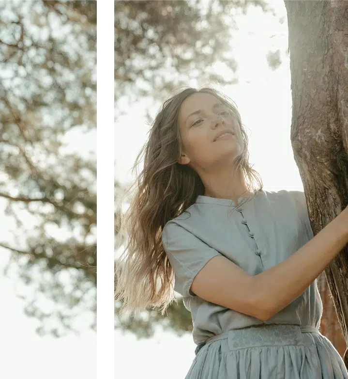  A woman embracing a tree with sunlight behind her, expressing grounding, peace, and emotional connection to nature.
