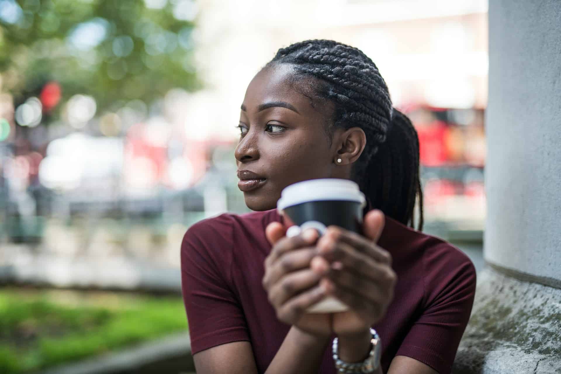 An african american woman drinking coffee out of a paper cup